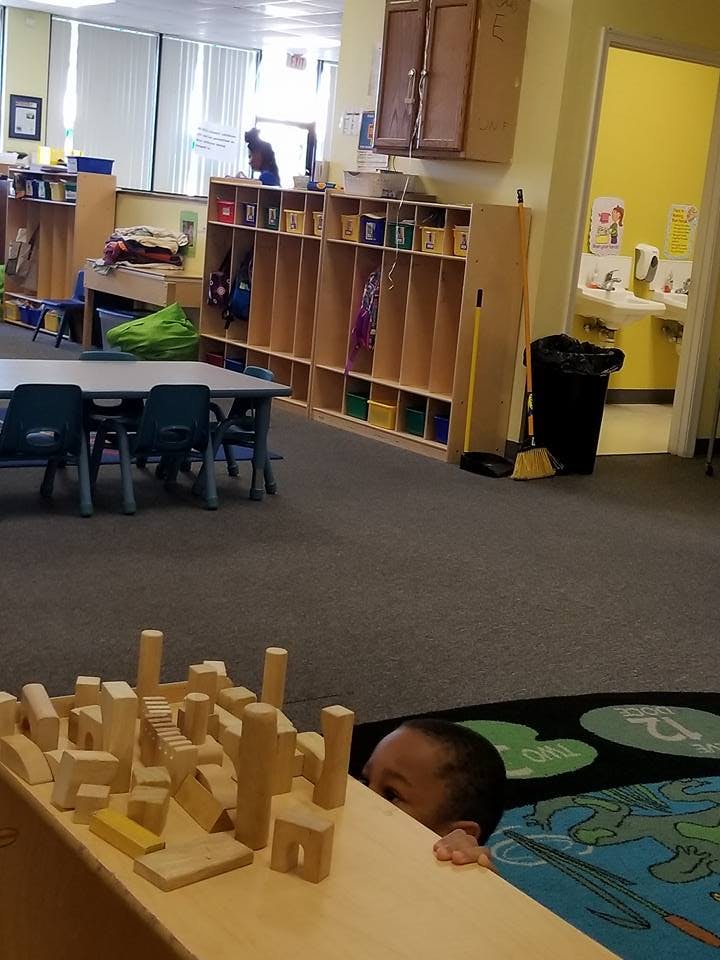 Child peeking over a table with wooden blocks in a classroom
