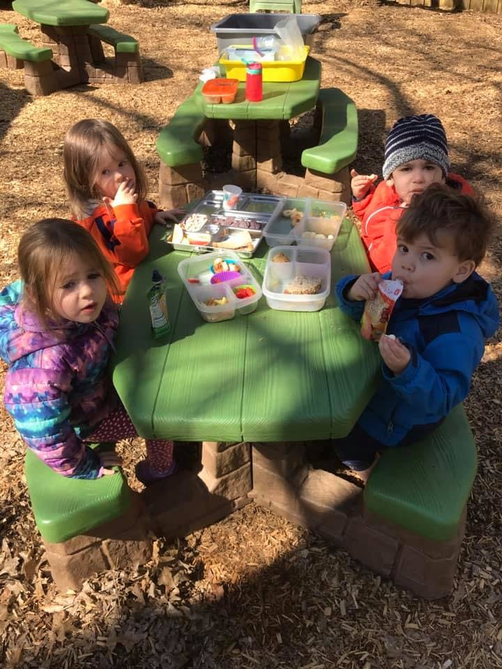 Four children eating at a picnic table outdoors