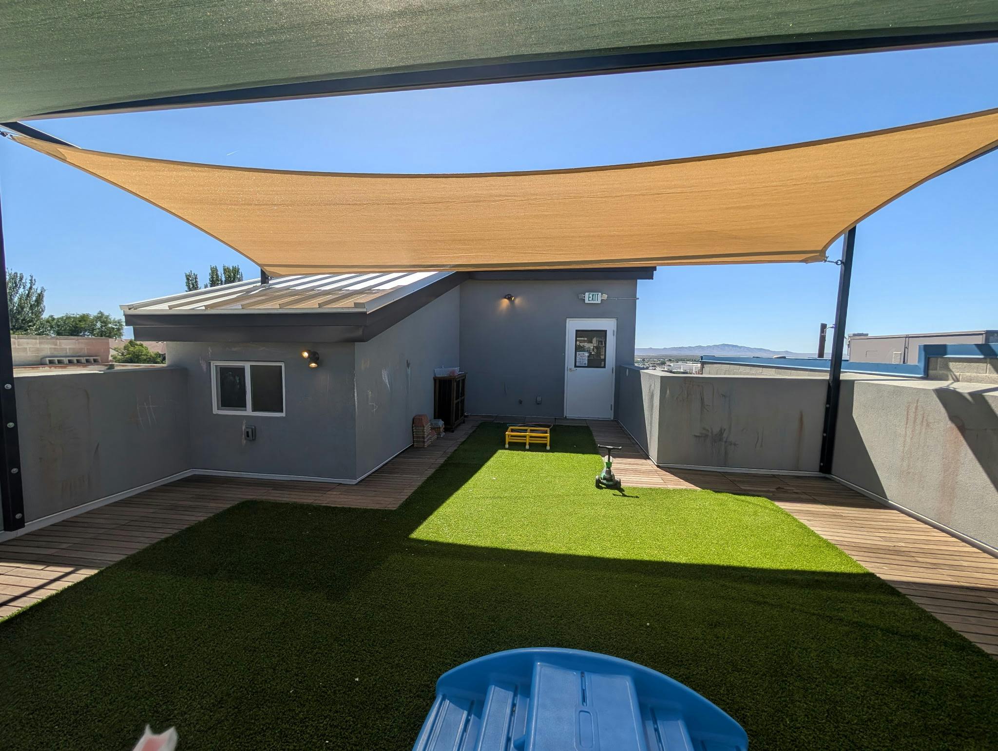 Rooftop deck with artificial turf, wooden planks, and shade sails