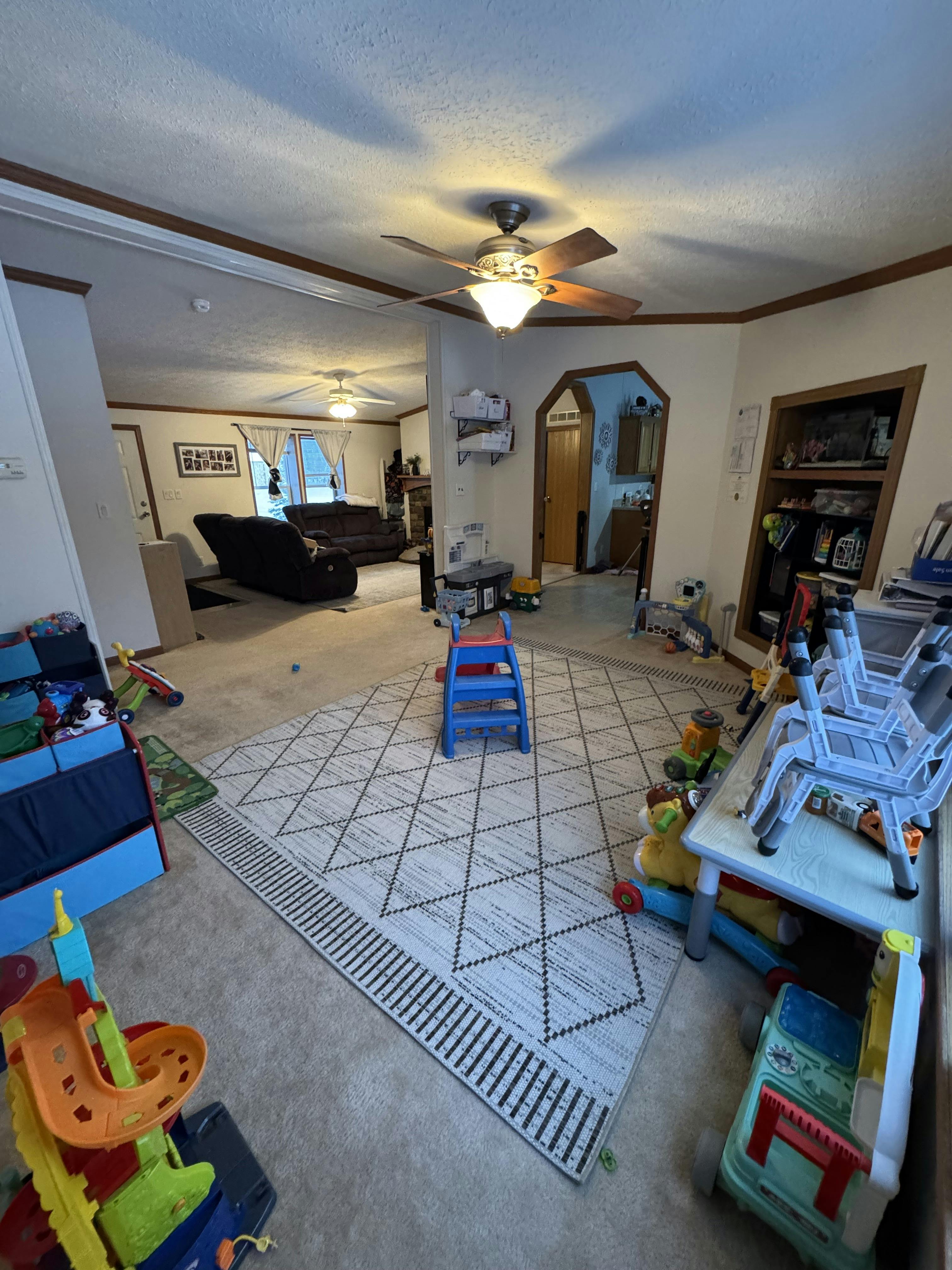 A room with toys on the floor, a blue step stool in the center, and a rug