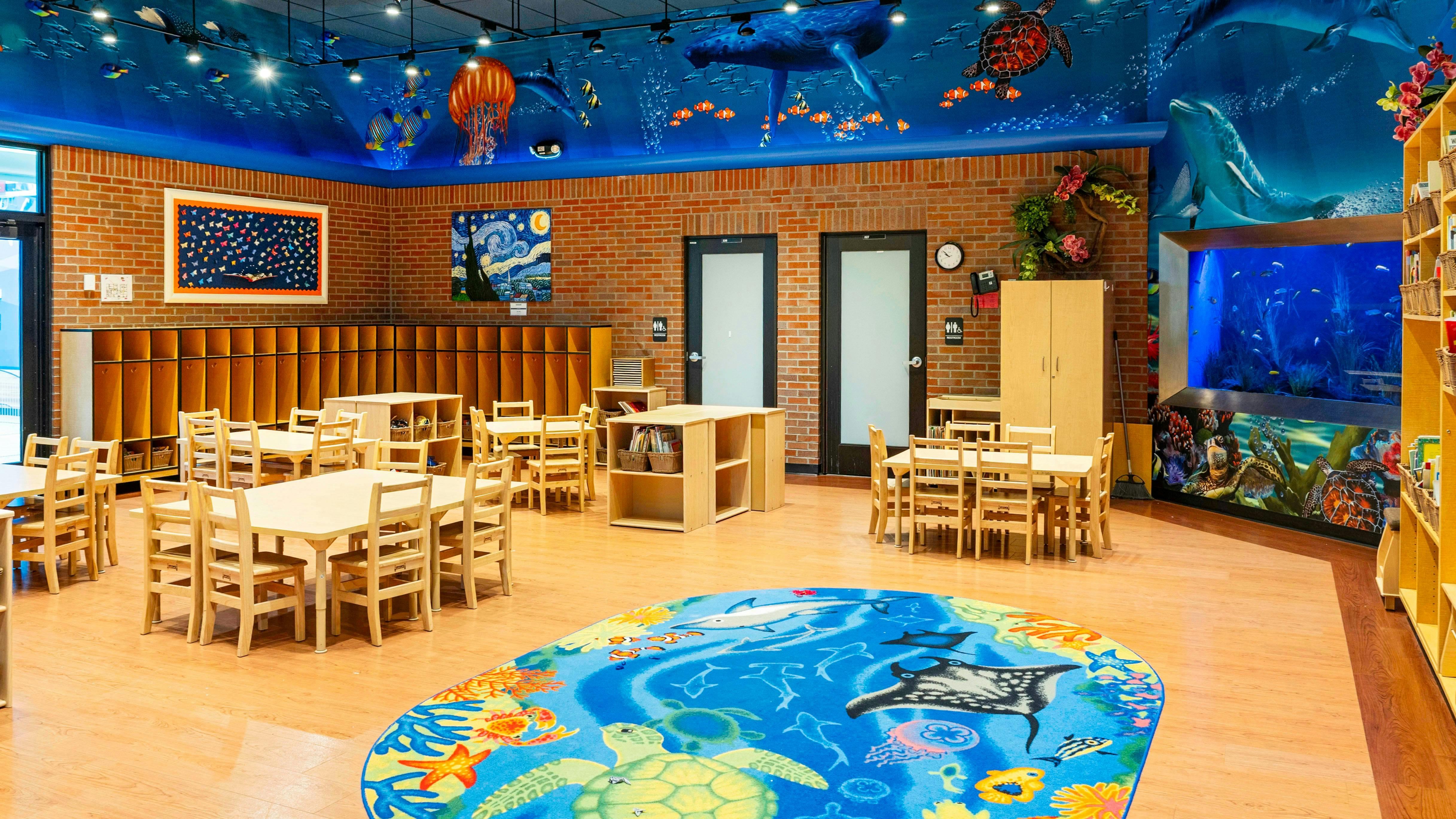 Classroom with small tables and chairs, ocean-themed mural, and aquarium