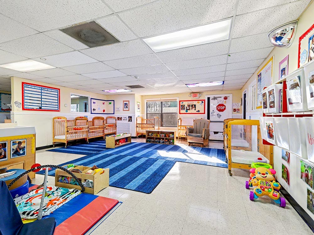 Empty infant nursery room with multiple cribs and a blue striped rug