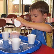 Child pouring from a cup into other cups on a tray