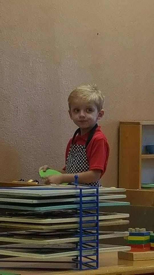 Child in a red shirt and checkered apron holding a green object