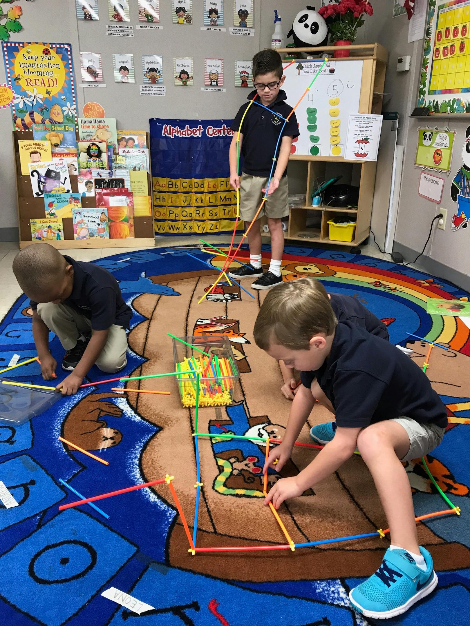 Three children playing with colorful building sticks on a rug in a classroom