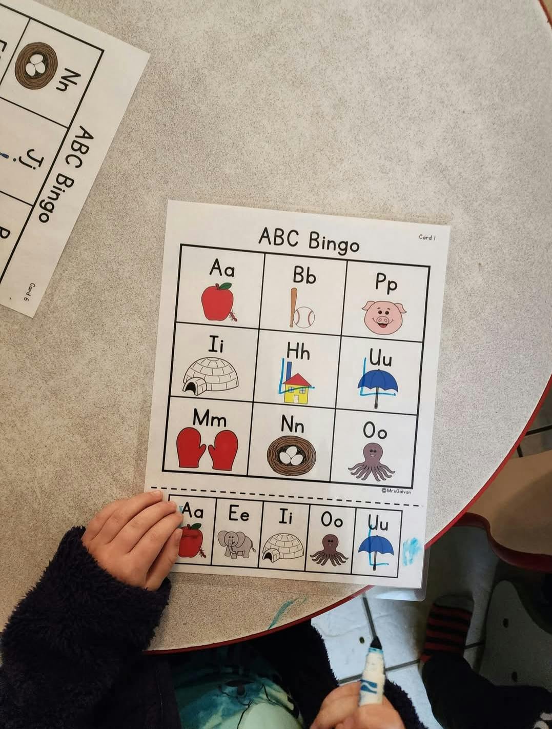 Child playing an ABC Bingo worksheet on a table