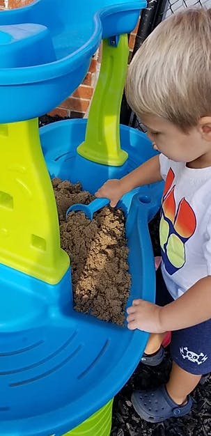 Child playing with sand and a blue shovel in a sand and water table
