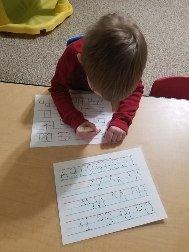 Child tracing letters and numbers on paper at a table