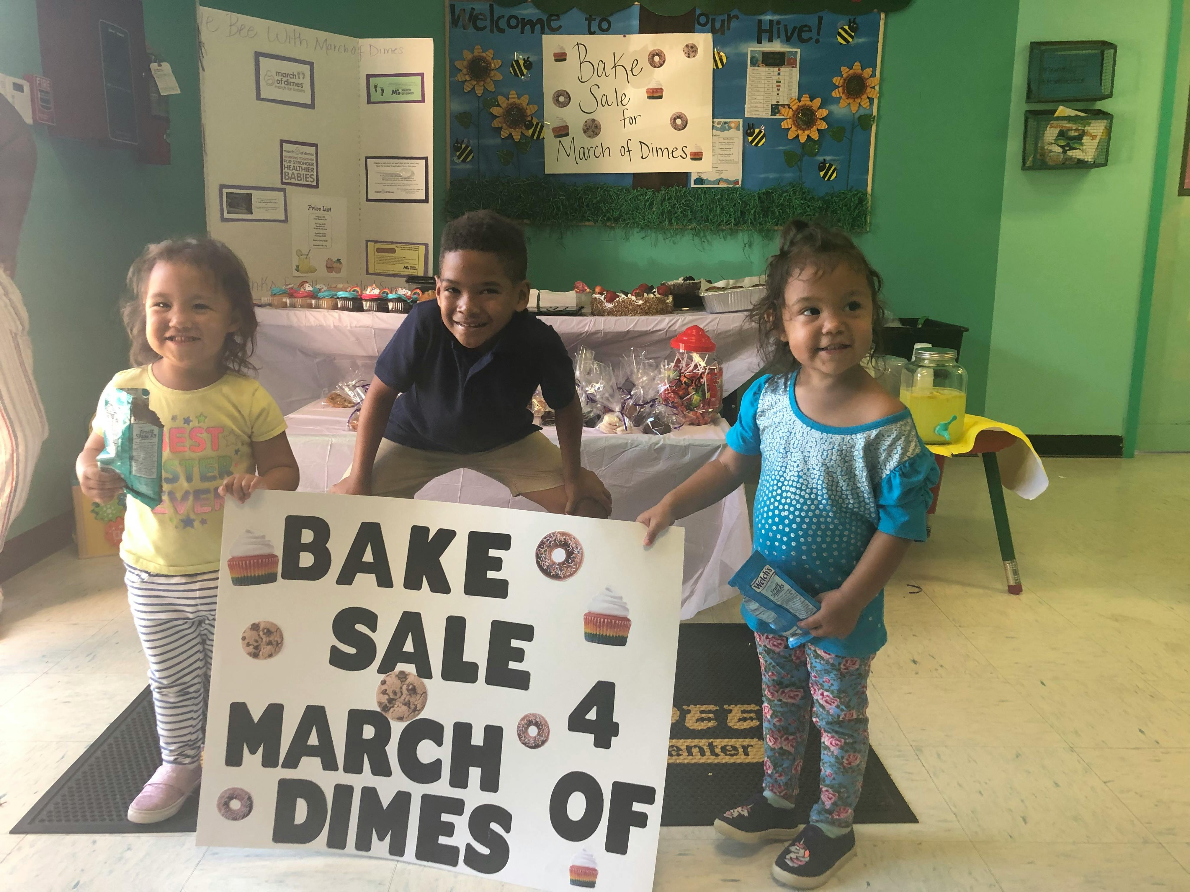 Three children holding a "Bake Sale for March of Dimes" sign