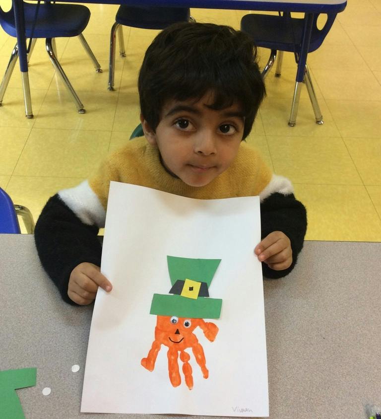 Child holding up a handprint art project in a classroom
