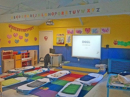 Classroom with nap mats on a colorful rug and a large screen