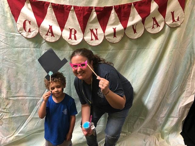 Person and child posing with props in-hand props in front of a carnival banner