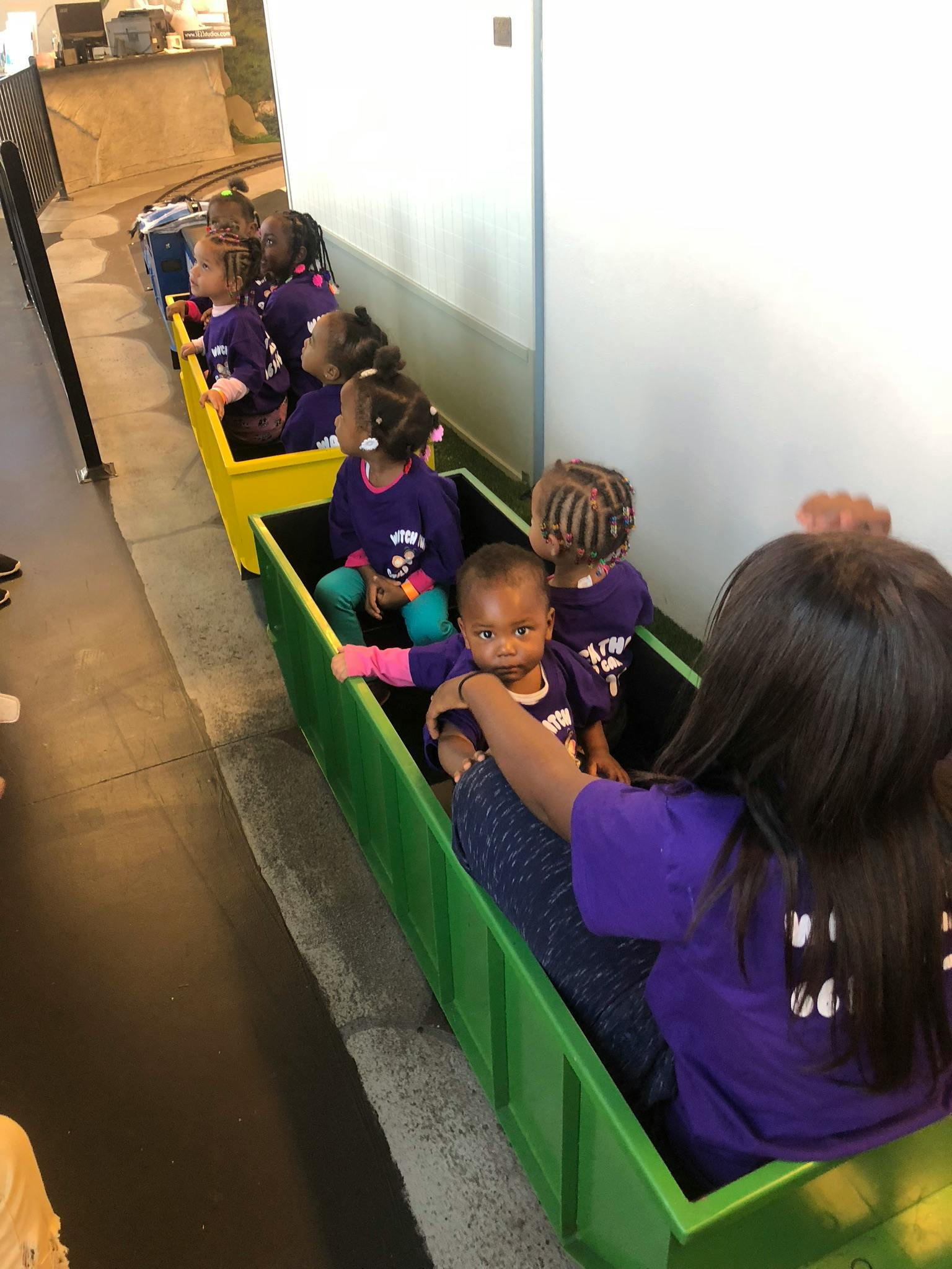 Children in purple shirts sitting in a line of colorful train cars