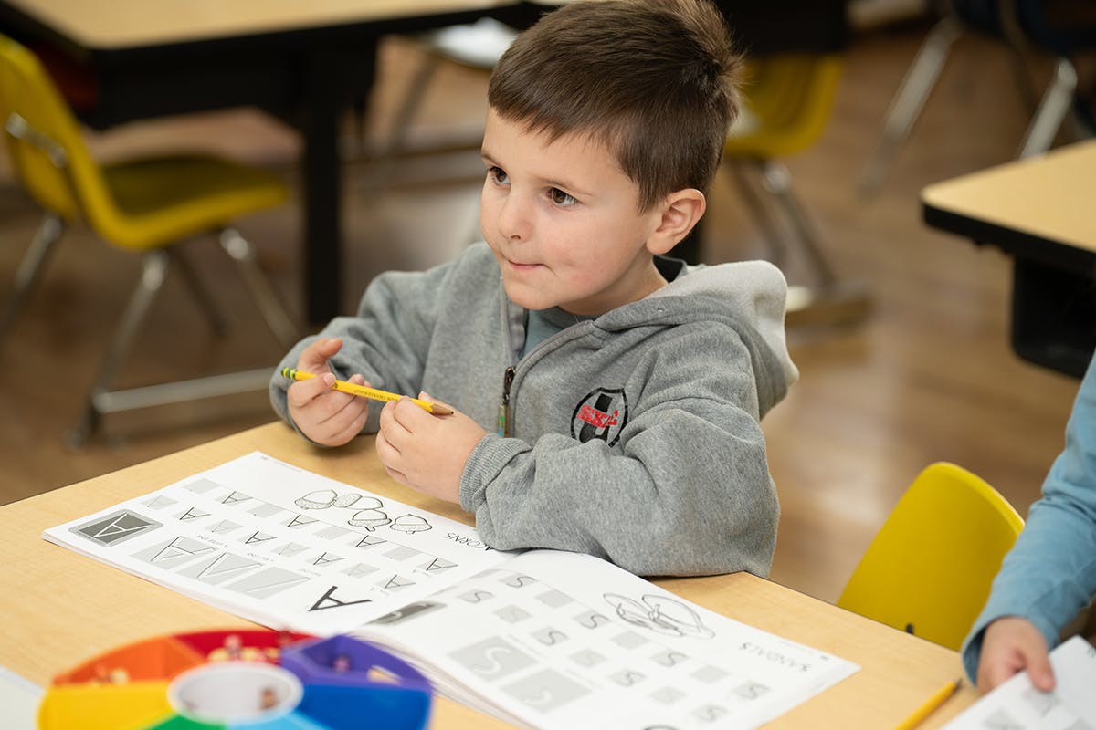 Child holding a pencil at a desk with a worksheet