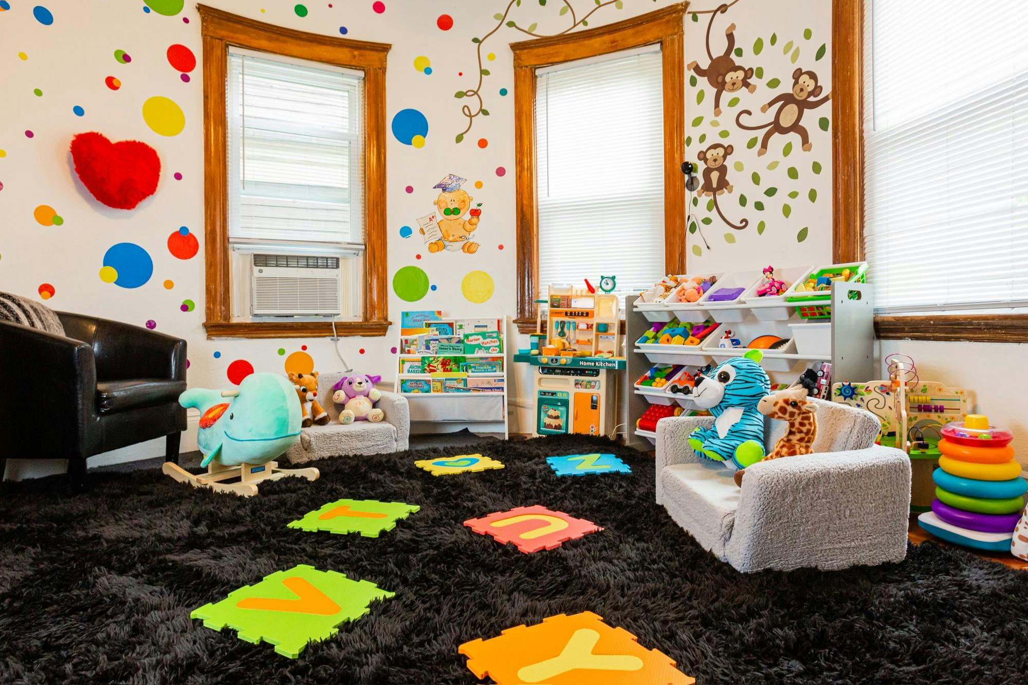 Playroom with colorful wall decals, toys, and alphabet floor mats