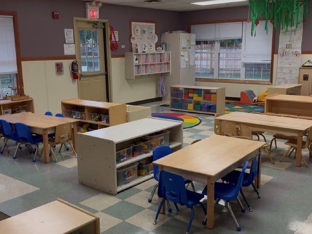 Empty classroom with small tables, chairs, and shelves full of toys