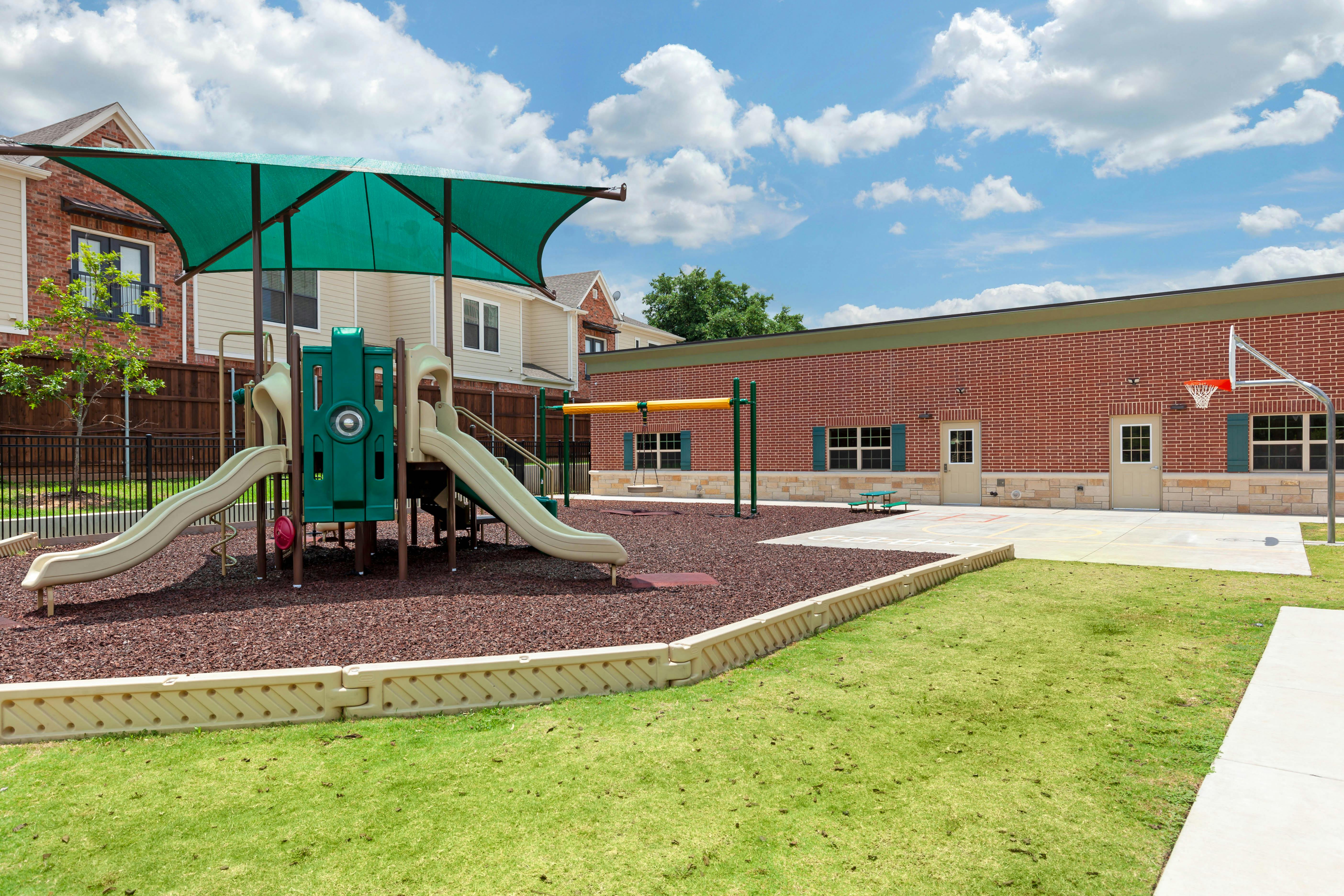 A colorful playground with slides and swings, a basketball hoop, and a brick building