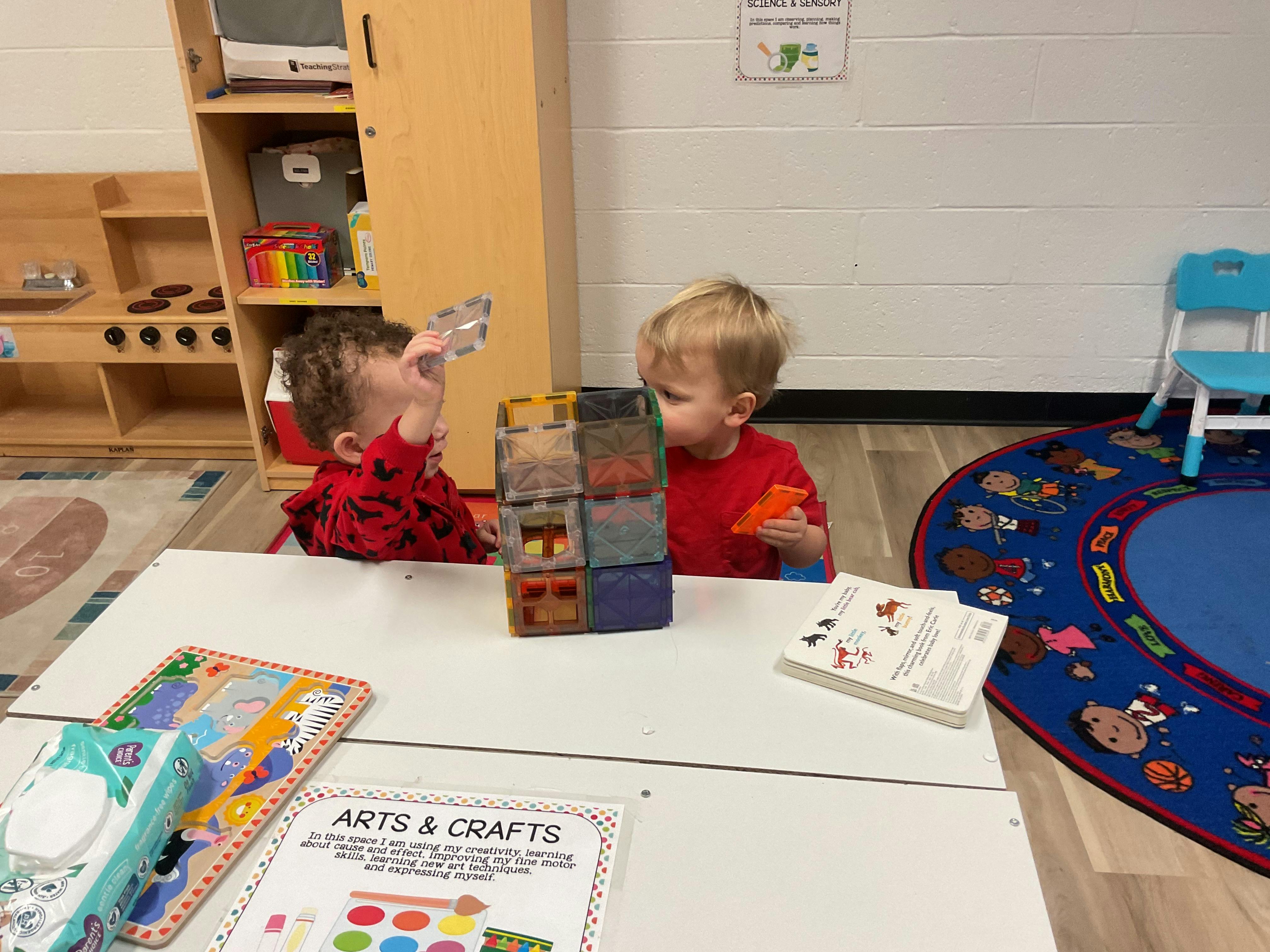 Two children playing with magnetic blocks on a white table in a classroom