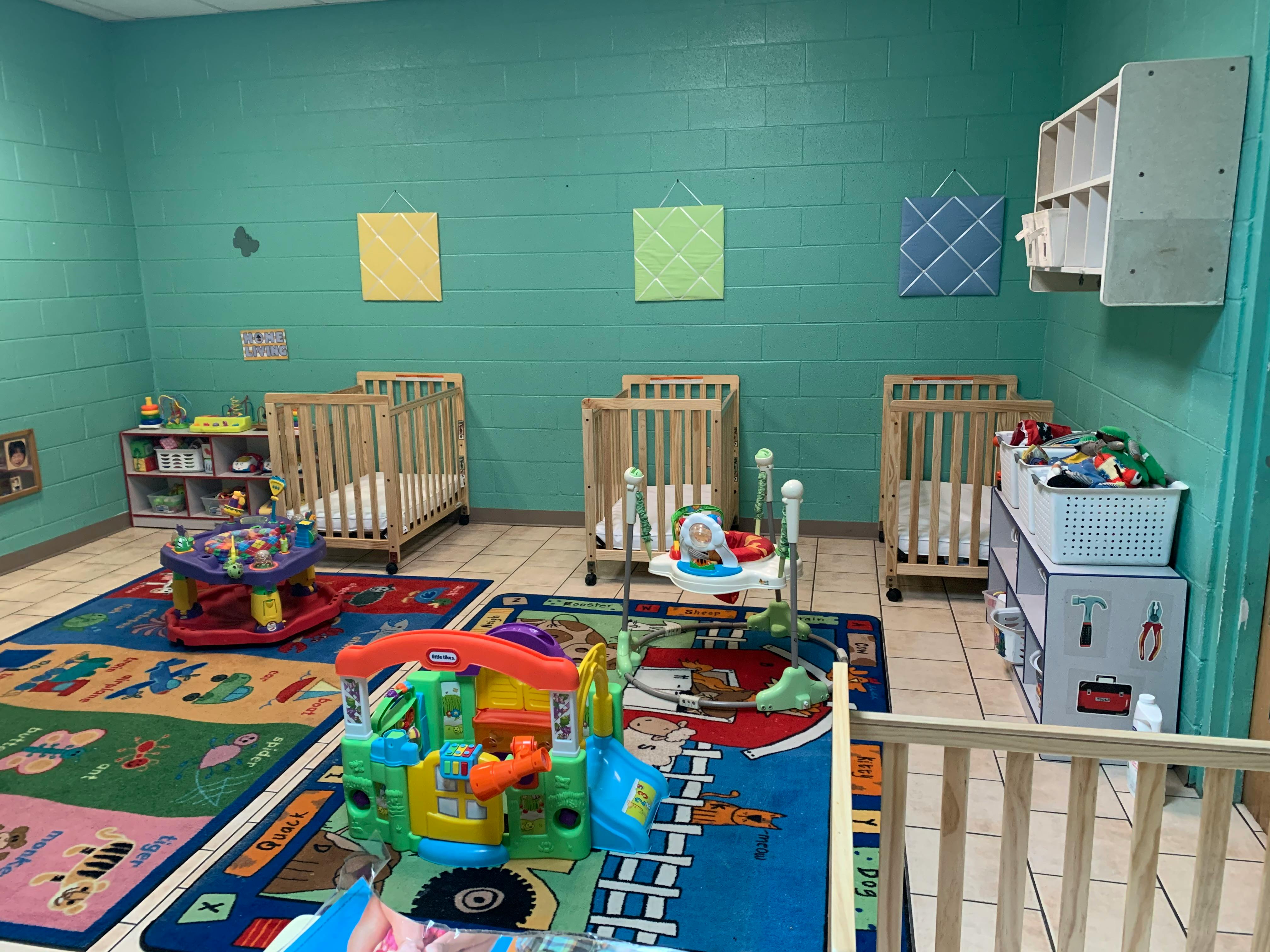 empty daycare room with multiple cribs, play mats, and toys
