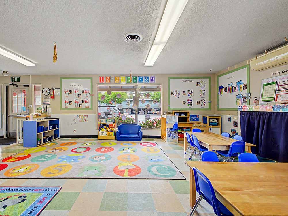 Classroom with tables, blue chairs, colorful rug, and child art on walls