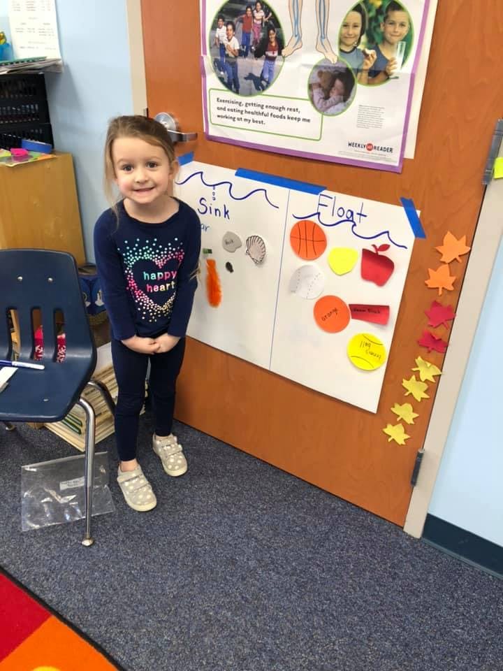 Child standing next to a science project board about sinking and floating