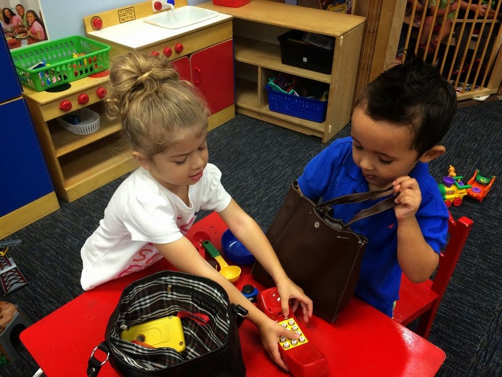 Two children playing with bags and toys at a red table in a classroom