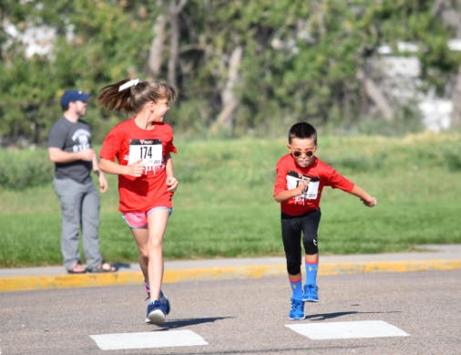 Two children running in a race with a person standing in the background