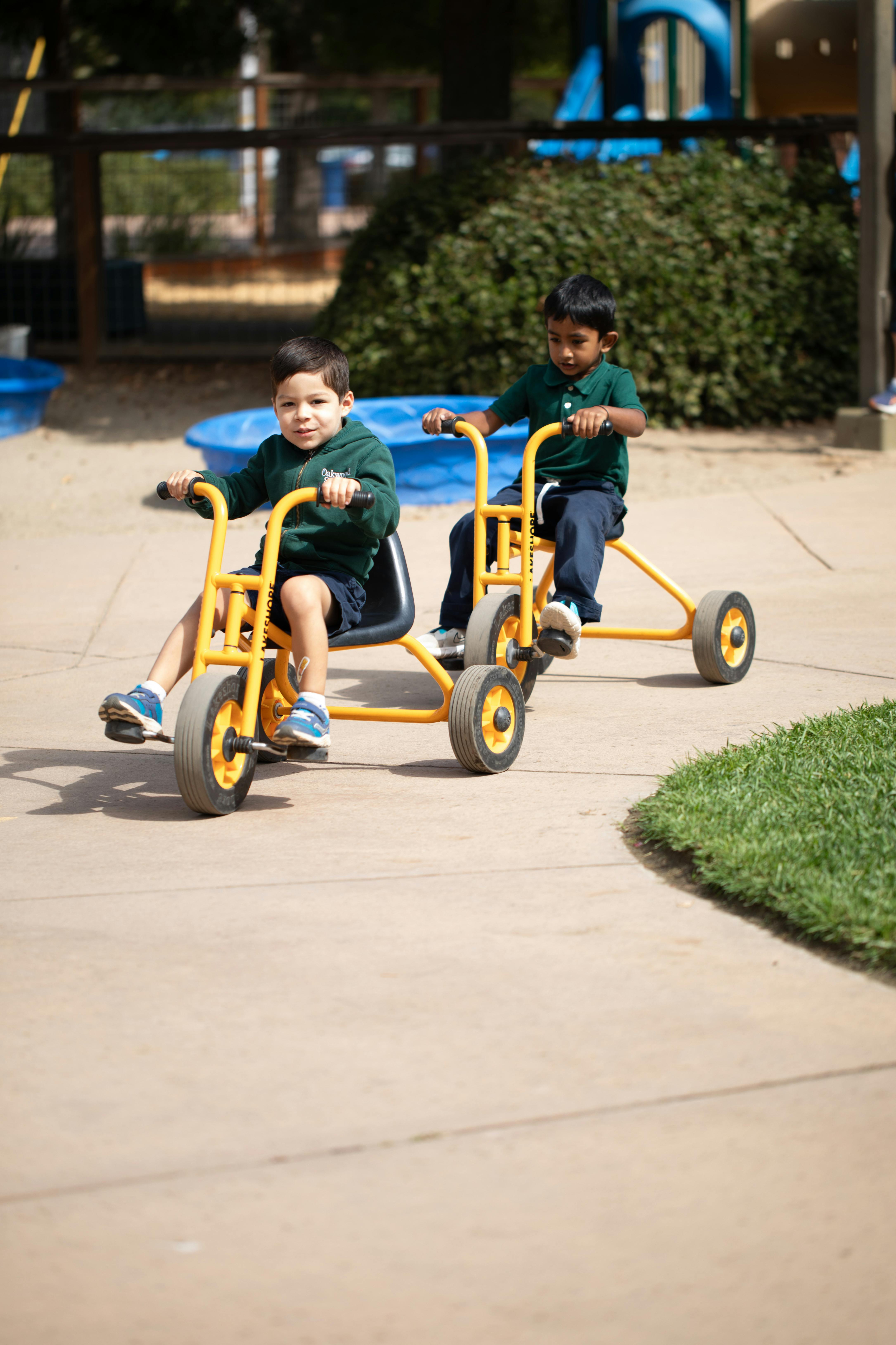 Two children riding side-by-side on yellow tricycles outdoors