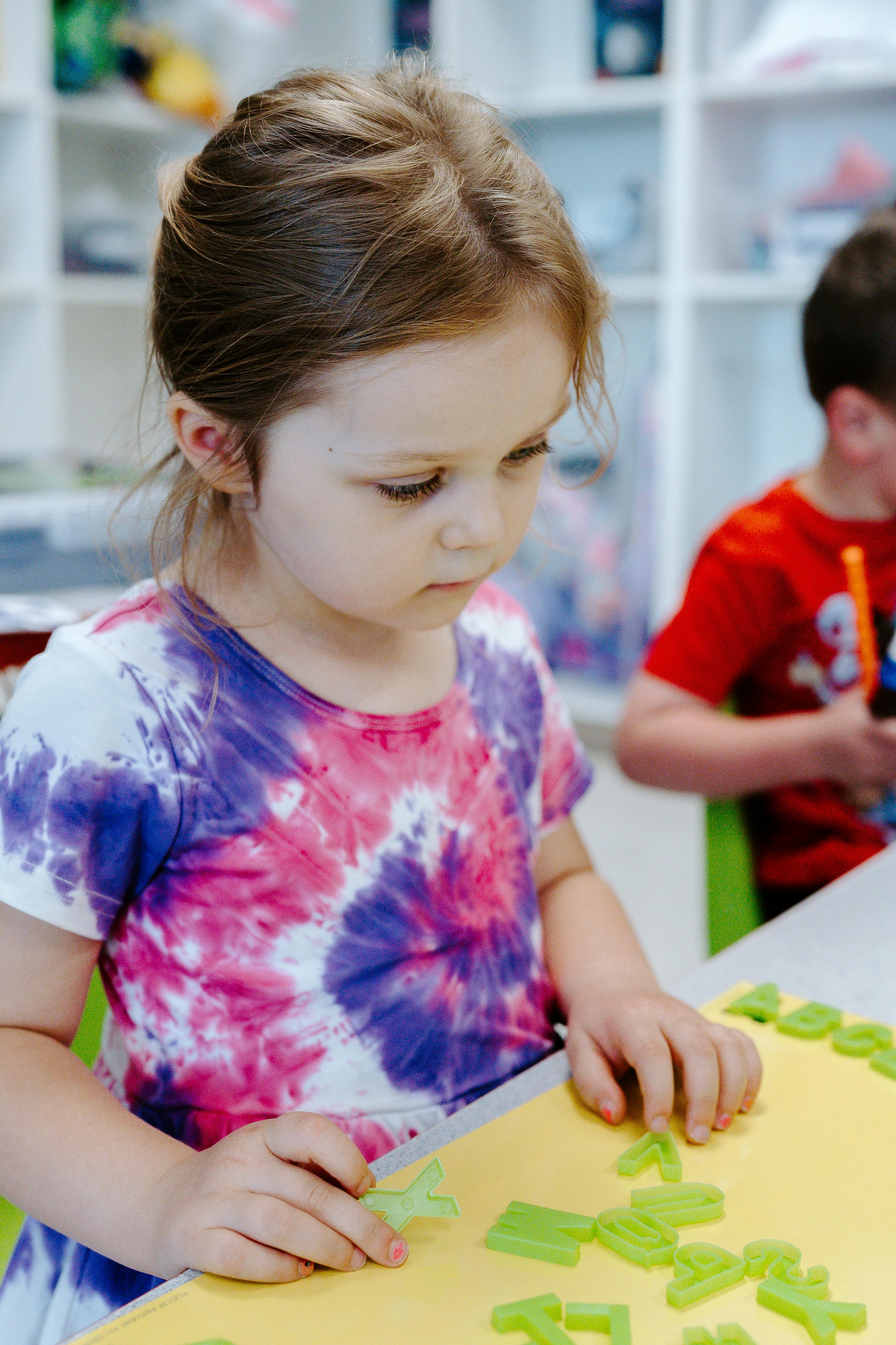 Child playing with green letter shapes on a yellow surface