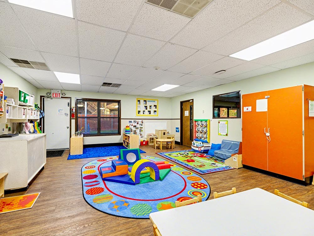 A colorful classroom with play mats and small chairs