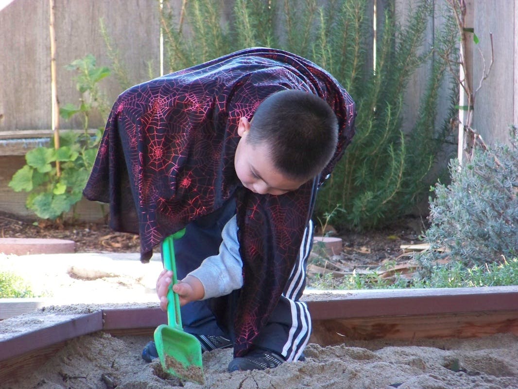 Child playing in sandbox with a green shovel