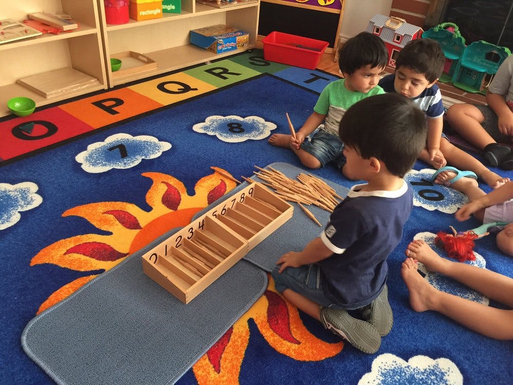 Children sitting on a rug with an alphabet border, playing with sticks and sorting sticks