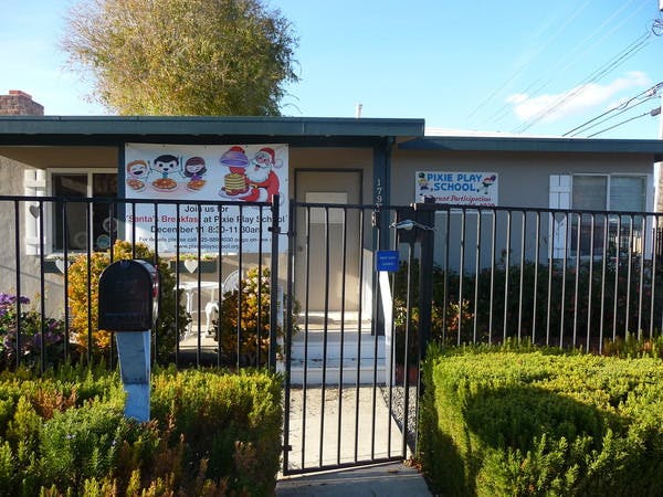 Building with a fence and a sign that reads "PINE PLAY SCHOOL"