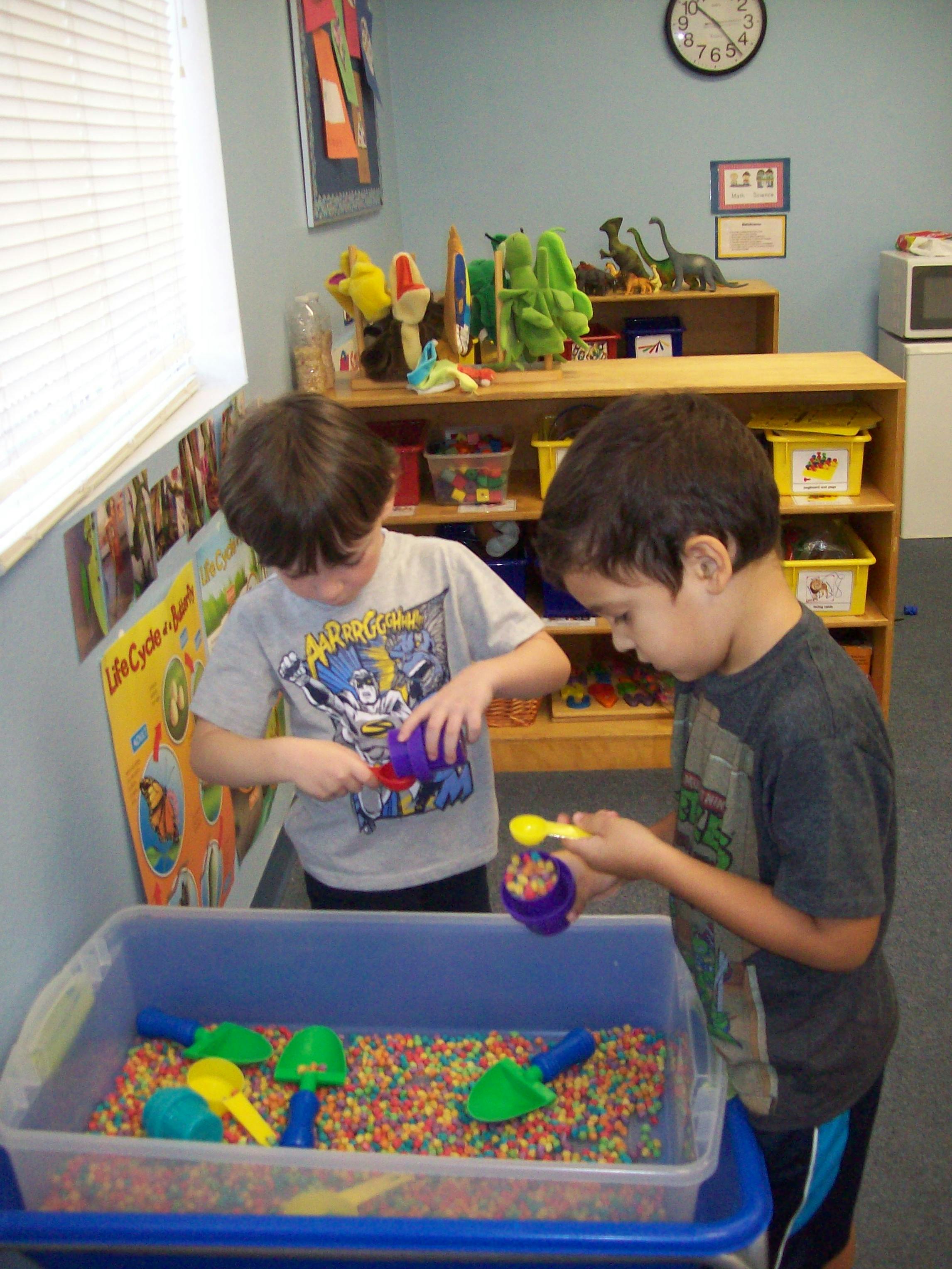 Two children playing with colorful beads in a sensory bin