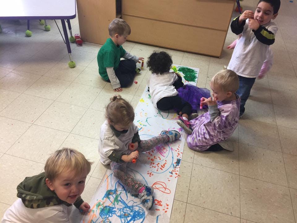 Multiple children sitting on the floor drawing on a long sheet of paper