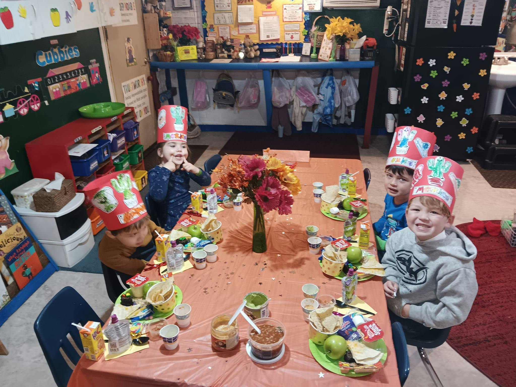 Children wearing paper hats sitting at a table with food and drinks