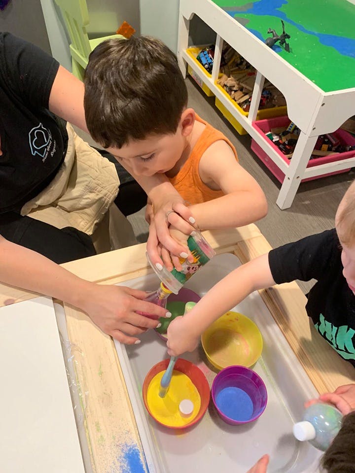 Adult and two children pouring and mixing sand in a tray