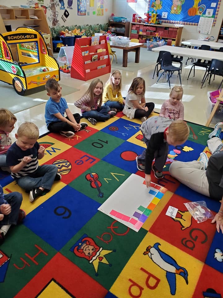 Children sitting on a colorful rug in a classroom