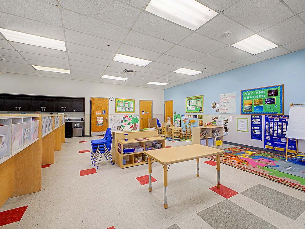Empty classroom with small tables and chairs, cubbies, and colorful rugs
