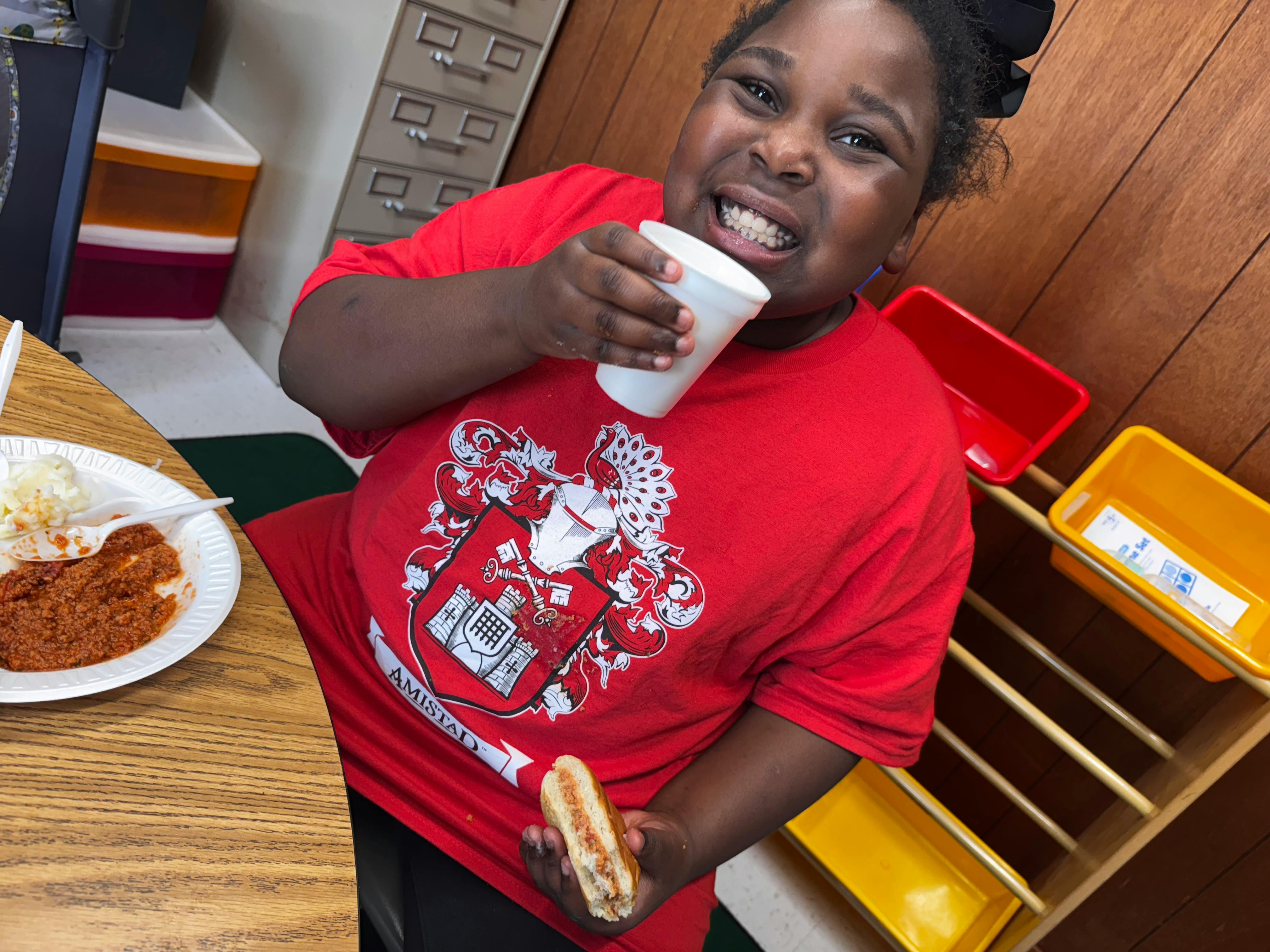 Child in red shirt holding a cup and a hot dog