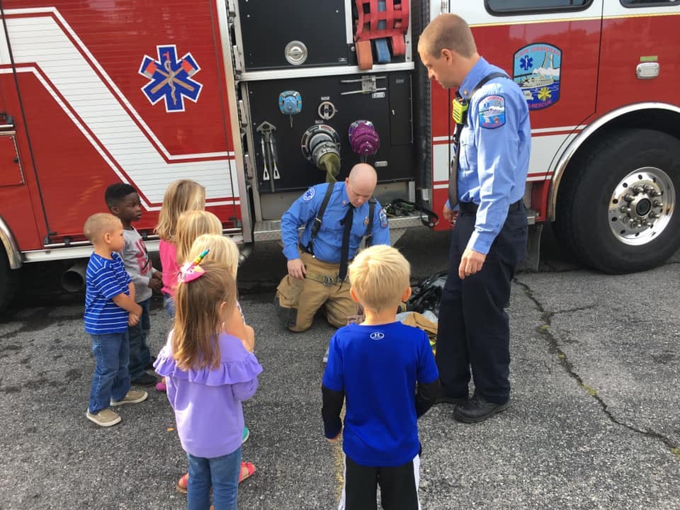 Two people in uniform with a group of children near a fire truck