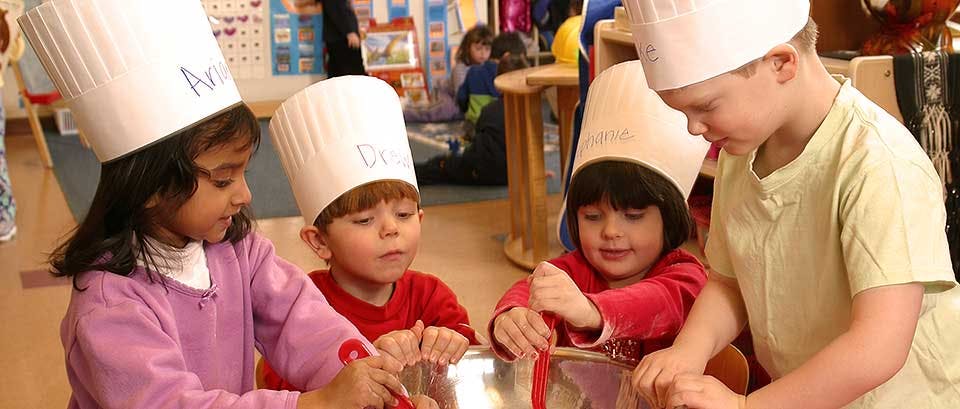 Four children wearing chef hats mixing ingredients in bowls