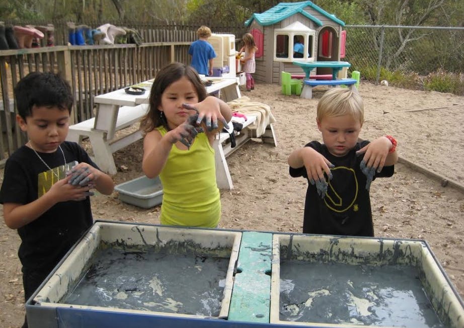 Three children playing with mud in a sandbox