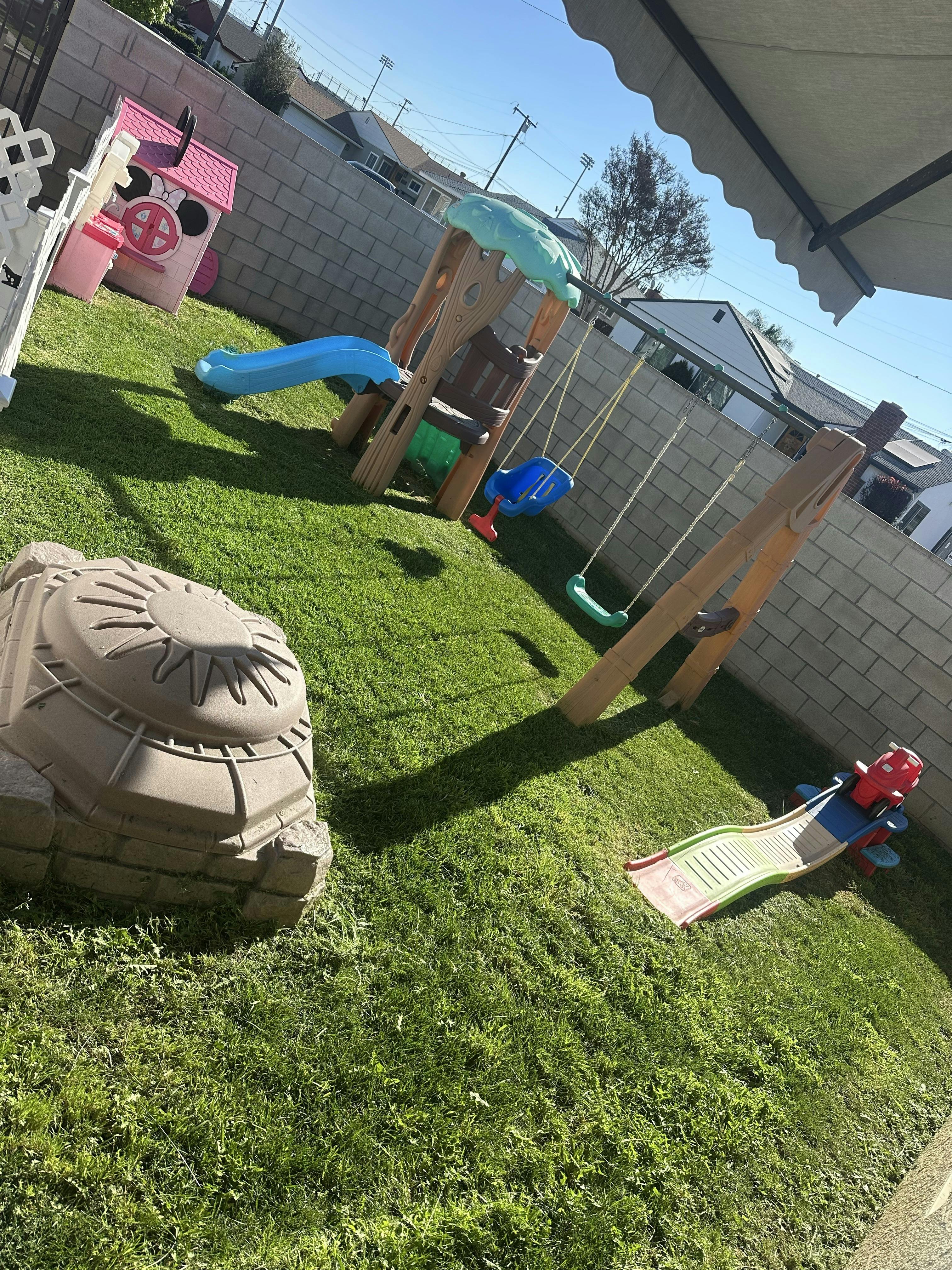 Playground with swings, slides, a small playhouse, and a sandbox on grass