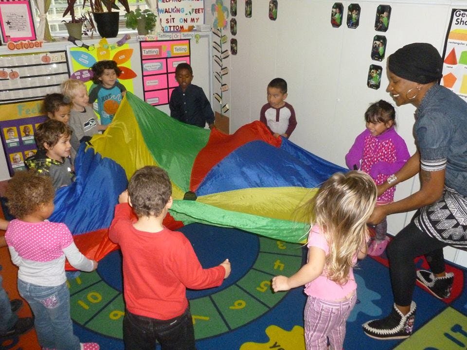 Adult and children playing with a colorful parachute in a classroom