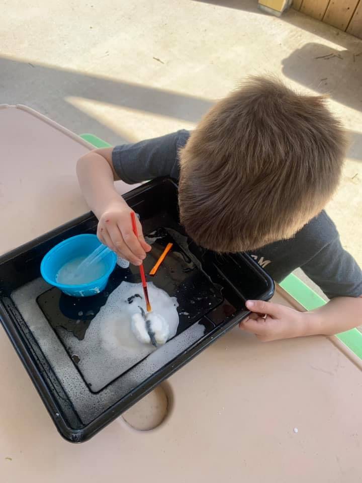 Child painting with a brush in a black tray with white foam