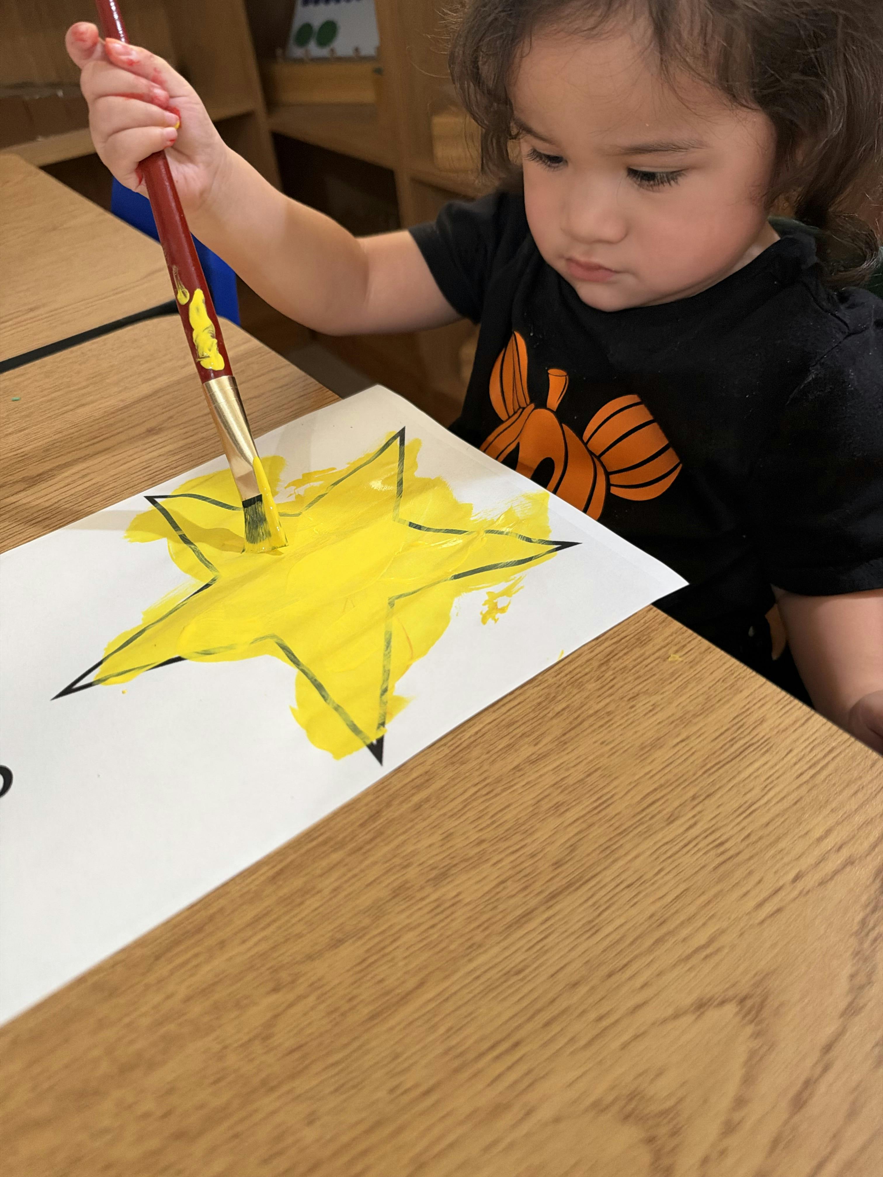 Child painting a yellow star on paper at a table