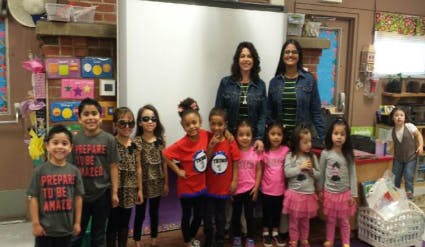 Two people and multiple children posing for a photo in a classroom