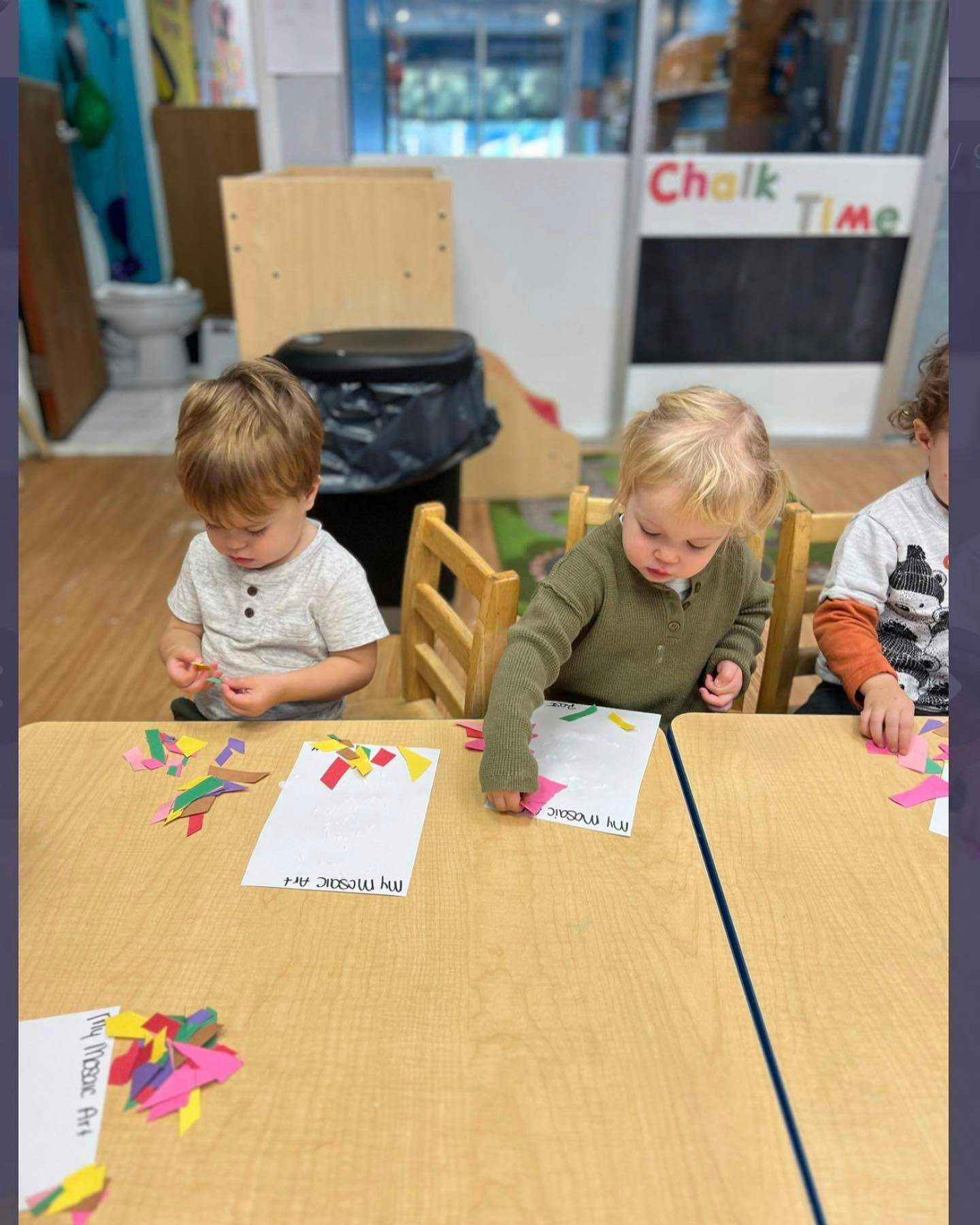 Three children doing crafts at a table in a classroom
