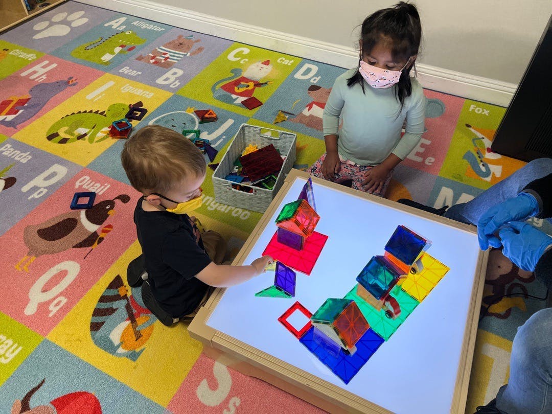 Two children playing with colorful blocks on a light table